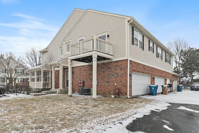 view of snow covered exterior featuring cooling unit, a balcony, and a garage