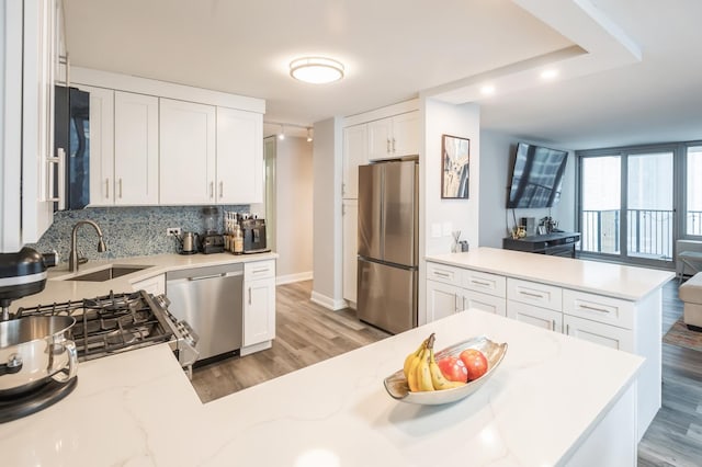 kitchen featuring appliances with stainless steel finishes, white cabinetry, sink, light stone counters, and kitchen peninsula