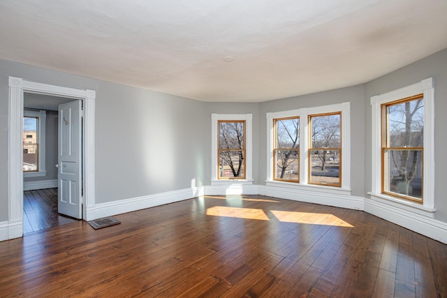 empty room with a healthy amount of sunlight, baseboards, and dark wood-style flooring