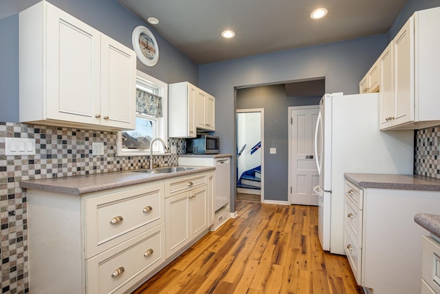 kitchen with tasteful backsplash, light wood-style flooring, white cabinets, a sink, and white appliances