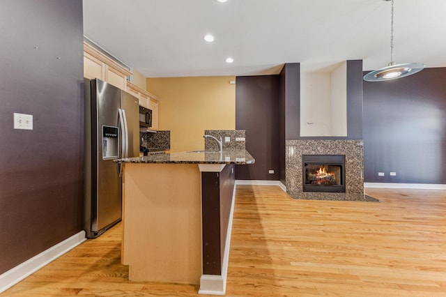 kitchen with decorative light fixtures, sink, stainless steel fridge, dark stone counters, and light hardwood / wood-style flooring