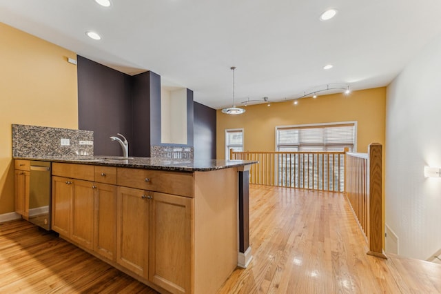 kitchen featuring decorative light fixtures, sink, dark stone countertops, and kitchen peninsula