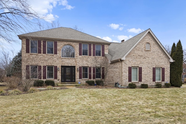 view of front of home featuring a front yard, brick siding, and a shingled roof