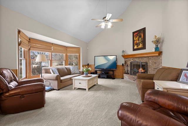 living room featuring a ceiling fan, high vaulted ceiling, wainscoting, a brick fireplace, and carpet flooring