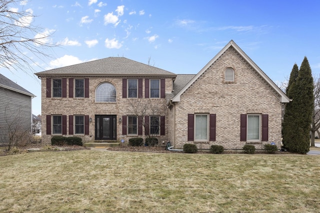 colonial house with brick siding, a front yard, and a shingled roof