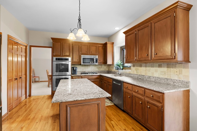 kitchen with a center island, decorative backsplash, appliances with stainless steel finishes, light wood-style floors, and hanging light fixtures