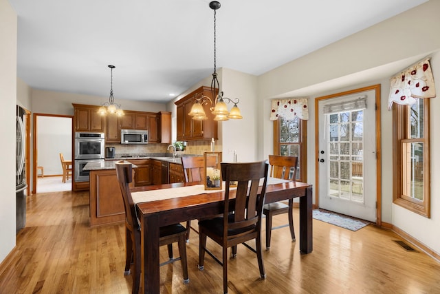 dining area featuring visible vents, baseboards, light wood-type flooring, and an inviting chandelier