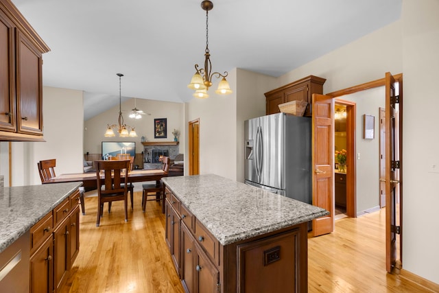 kitchen with light wood finished floors, a kitchen island, stainless steel fridge with ice dispenser, a stone fireplace, and hanging light fixtures