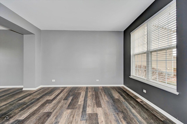 spare room with baseboards and dark wood-type flooring