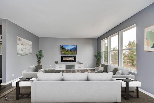 living area with a glass covered fireplace, dark wood-type flooring, and baseboards