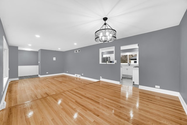 unfurnished living room featuring a notable chandelier and light wood-type flooring