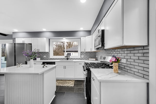 kitchen featuring white cabinetry, a center island, dark tile patterned flooring, stainless steel appliances, and light stone countertops