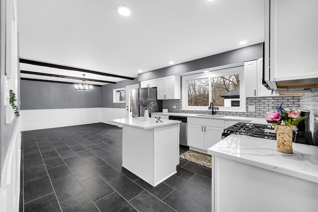 kitchen with sink, white cabinetry, stainless steel appliances, a center island, and light stone counters