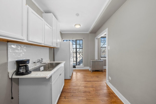 kitchen with light wood finished floors, tasteful backsplash, radiator heating unit, white cabinetry, and a sink