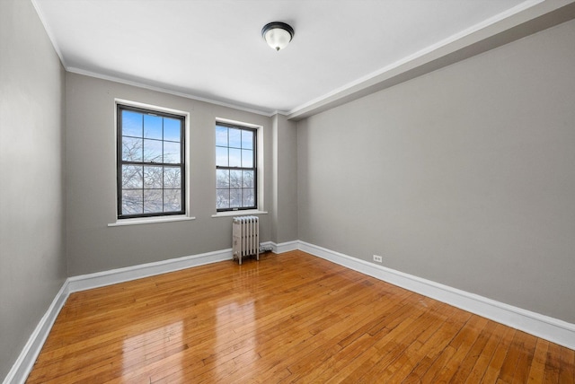 spare room with ornamental molding, radiator heating unit, wood-type flooring, and baseboards