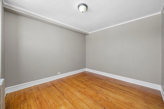 unfurnished room featuring wood-type flooring, baseboards, radiator heating unit, and crown molding