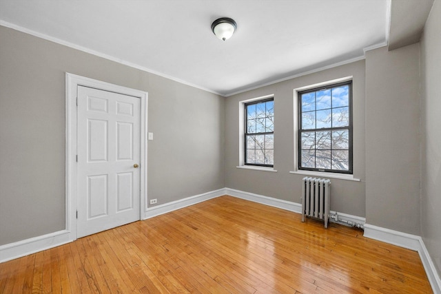 spare room with radiator, light wood-type flooring, baseboards, and crown molding