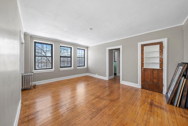 unfurnished living room with built in features, crown molding, hardwood / wood-style floors, radiator heating unit, and baseboards