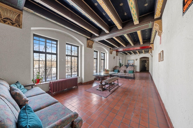 tiled living area featuring arched walkways, a textured wall, radiator heating unit, and beam ceiling