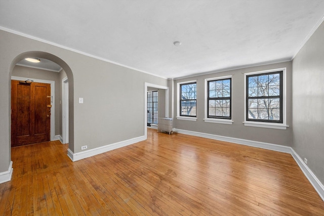 spare room with light wood-style floors, arched walkways, crown molding, and baseboards