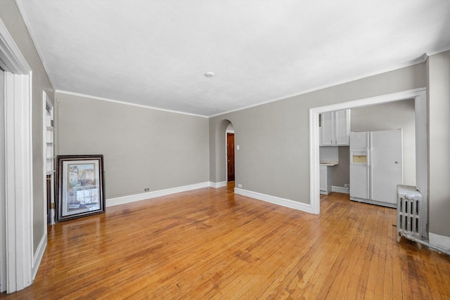 unfurnished living room featuring arched walkways, crown molding, light wood-style flooring, radiator heating unit, and baseboards