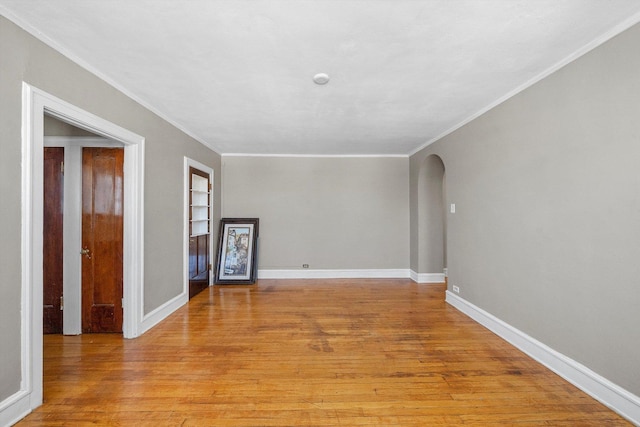 unfurnished room with arched walkways, ornamental molding, baseboards, and light wood-style floors