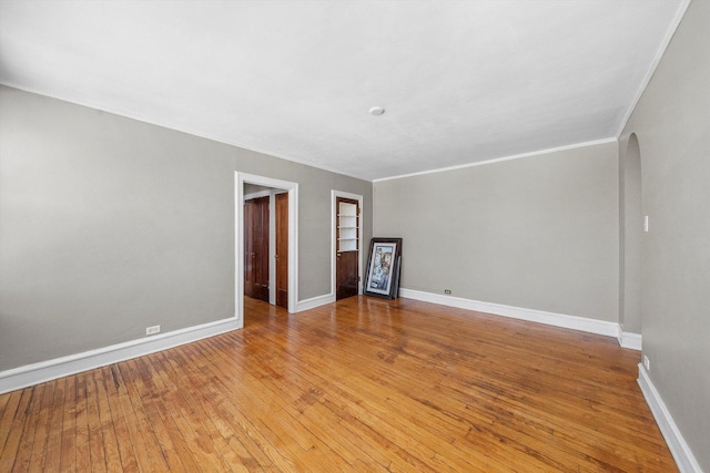 empty room with arched walkways, ornamental molding, light wood-type flooring, and baseboards