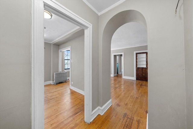 hall with arched walkways, baseboards, ornamental molding, light wood-type flooring, and radiator