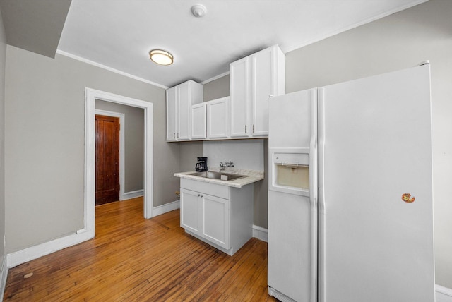 kitchen featuring white fridge with ice dispenser, white cabinetry, a sink, and light wood-style flooring