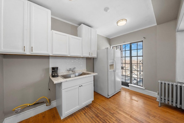 kitchen with white cabinets, radiator, light countertops, white fridge with ice dispenser, and a sink