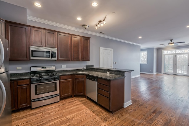 kitchen with crown molding, light hardwood / wood-style flooring, dark stone countertops, stainless steel appliances, and kitchen peninsula