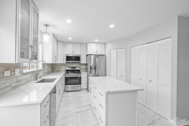 kitchen with pendant lighting, sink, appliances with stainless steel finishes, white cabinetry, and a center island