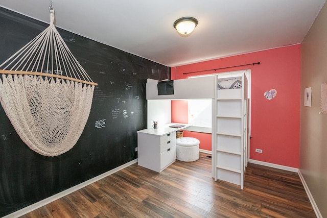 bedroom with baseboards, wood finished floors, and an accent wall