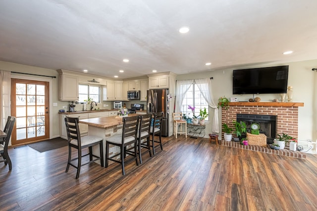 dining room with dark wood-style floors, a healthy amount of sunlight, and a brick fireplace