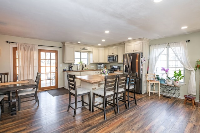 kitchen with dark wood-type flooring, baseboards, recessed lighting, appliances with stainless steel finishes, and a kitchen breakfast bar