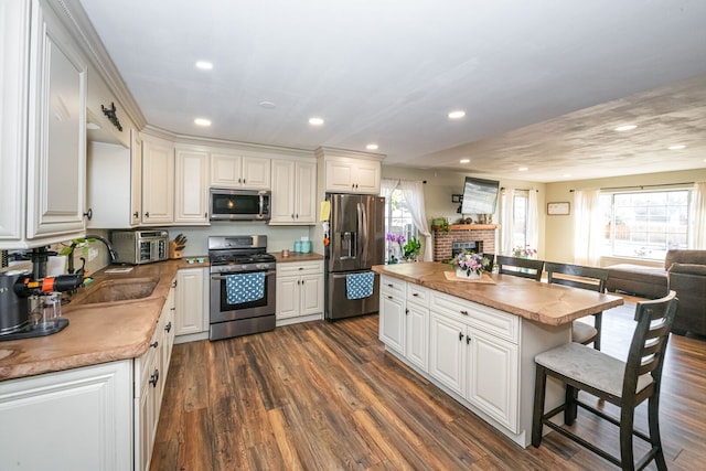 kitchen with butcher block counters, a breakfast bar, dark wood-style floors, white cabinets, and stainless steel appliances