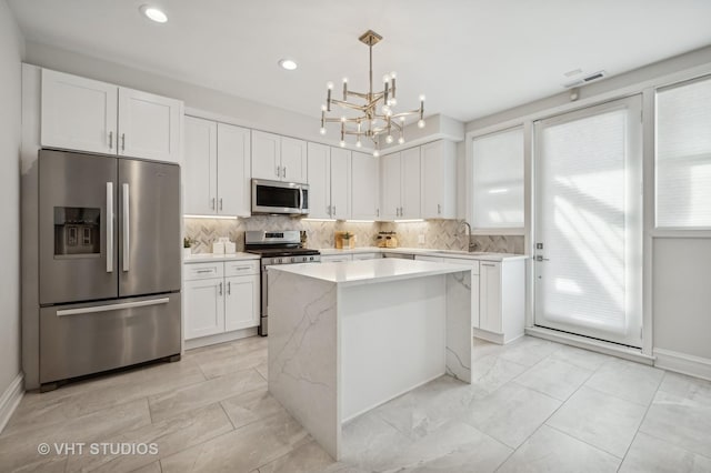 kitchen with stainless steel appliances, a kitchen island, white cabinets, tasteful backsplash, and pendant lighting