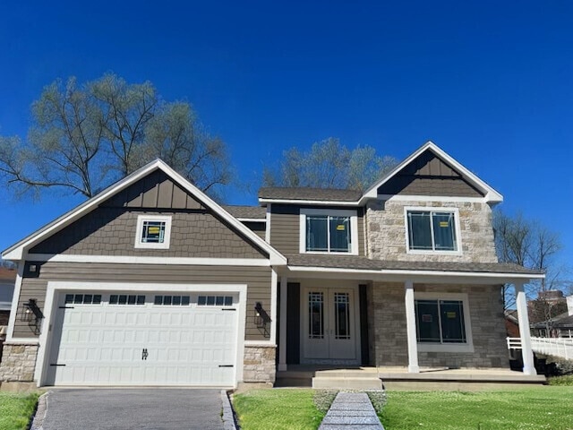 craftsman-style house with a porch, an attached garage, driveway, stone siding, and board and batten siding