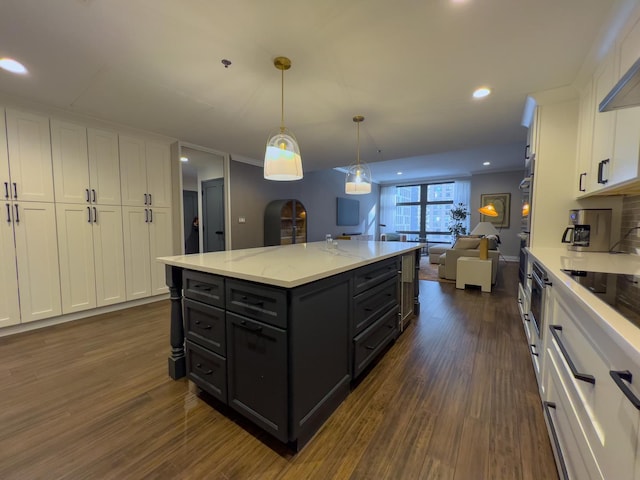 kitchen featuring dark wood-type flooring, hanging light fixtures, light stone counters, white cabinets, and a kitchen island