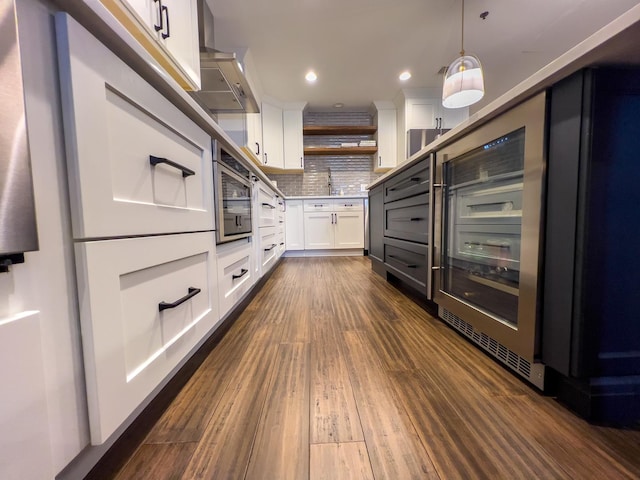 kitchen with hanging light fixtures, tasteful backsplash, white cabinets, oven, and wall chimney exhaust hood