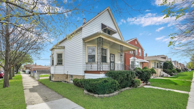 view of front of house with covered porch, a chimney, a front yard, and fence