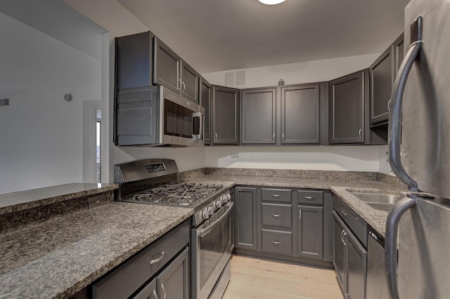 kitchen featuring light hardwood / wood-style flooring, dark stone counters, kitchen peninsula, and appliances with stainless steel finishes