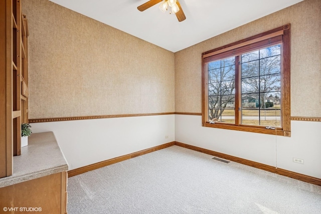 carpeted spare room with wallpapered walls, baseboards, visible vents, and ceiling fan