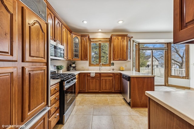 kitchen with light countertops, appliances with stainless steel finishes, a sink, and brown cabinets