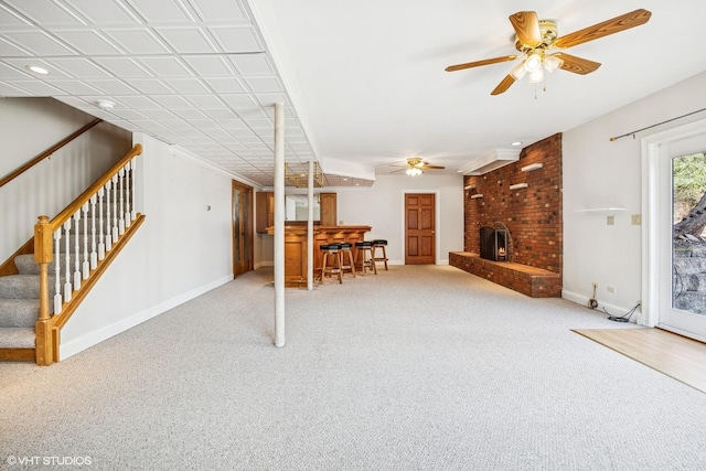 unfurnished living room with baseboards, ceiling fan, stairs, carpet flooring, and a fireplace