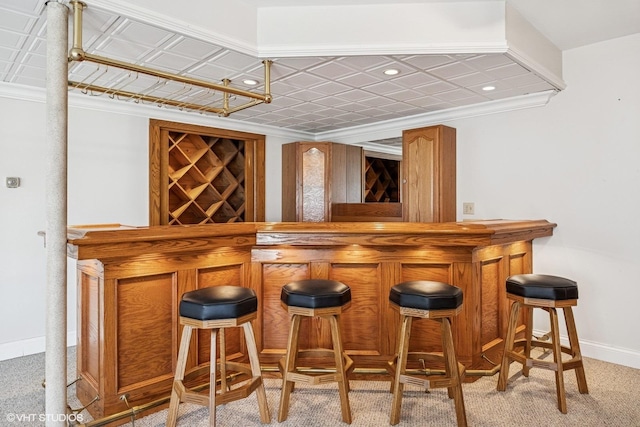 bar featuring light carpet, baseboards, a bar, an ornate ceiling, and crown molding