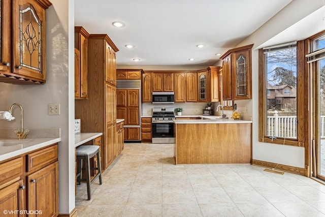 kitchen featuring glass insert cabinets, appliances with stainless steel finishes, brown cabinets, a peninsula, and light countertops