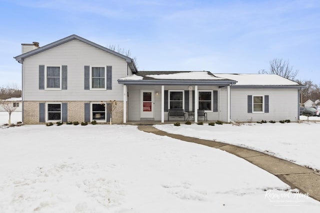 split level home featuring brick siding, covered porch, and a chimney