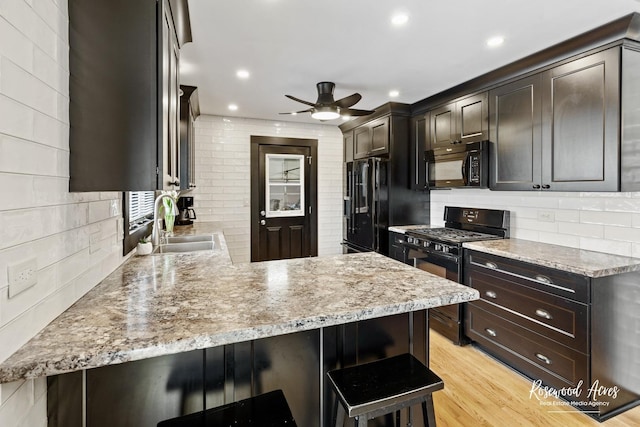 kitchen featuring black appliances, light wood-type flooring, backsplash, and a sink