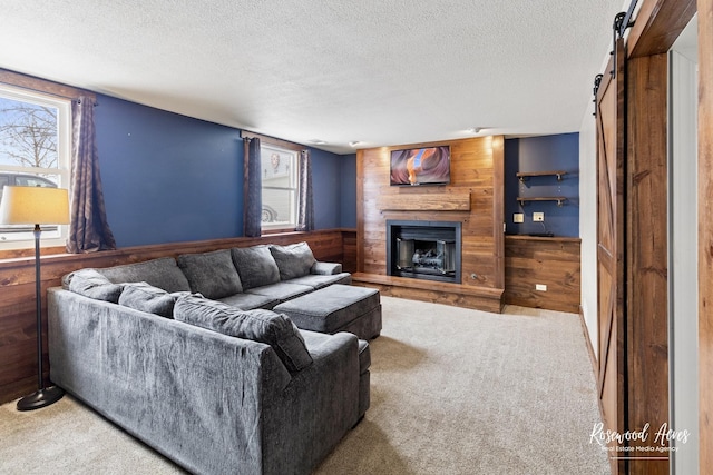 carpeted living area with a wainscoted wall, a textured ceiling, a barn door, wooden walls, and a fireplace